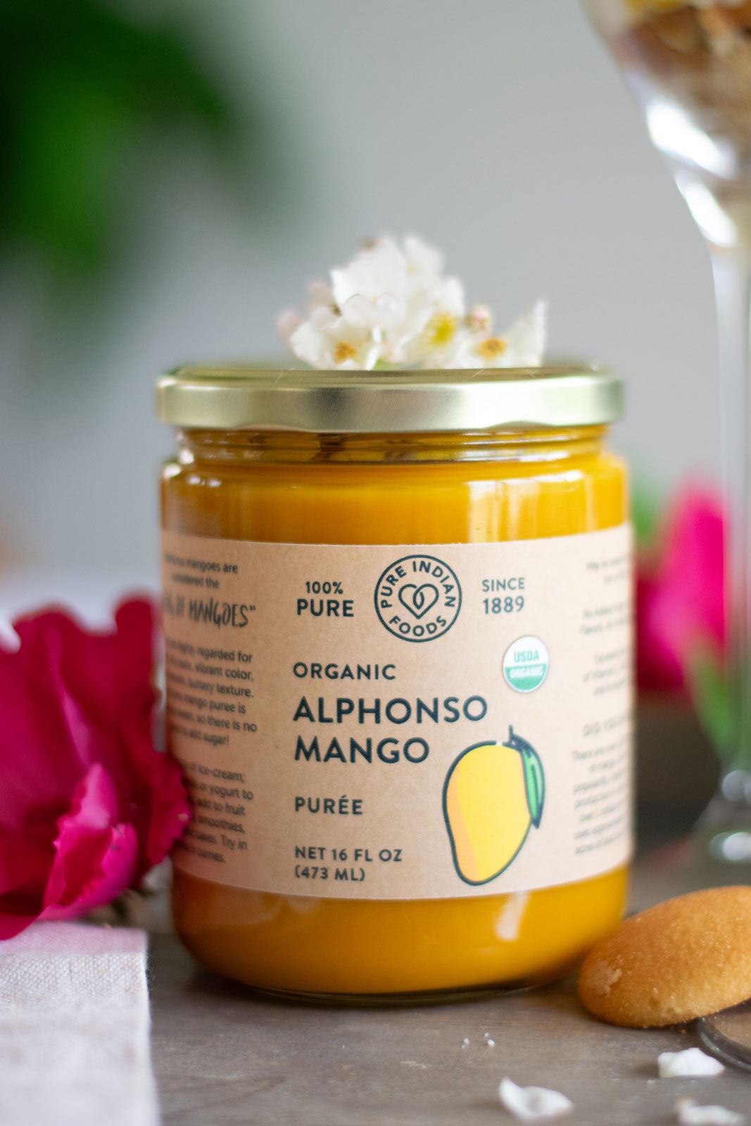 jar of organic alphonso mango puree containing 100% pure organic mango pulp displayed next to flowers