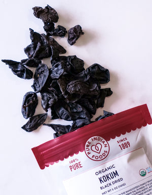 A bag of Pure Indian Foods Organic Kokum, opened and showing the dried, black kokum bits spilled onto a white surface.