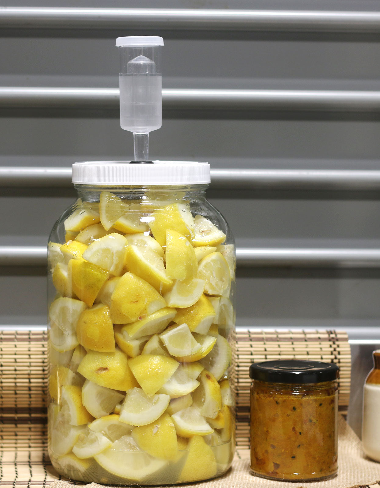 A small batch of our slow-fermented lemons in their fermentation vessel, next to a jar of our indian lemon pickle