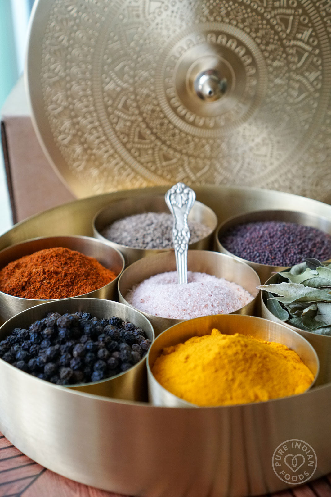 An open Gold Mandala Masala Dabba, made of solid brass, showing a beautiful collection of organic spices