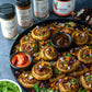 A tray of scrumptious pinwheels made with Pure Indian Foods products, including Organic Coriander Seed, Organic Kashmiri Chili Powder, Organic Cumin Seed, and Organic Tamarind Paste, all of which are displayed behind the pinwheels.