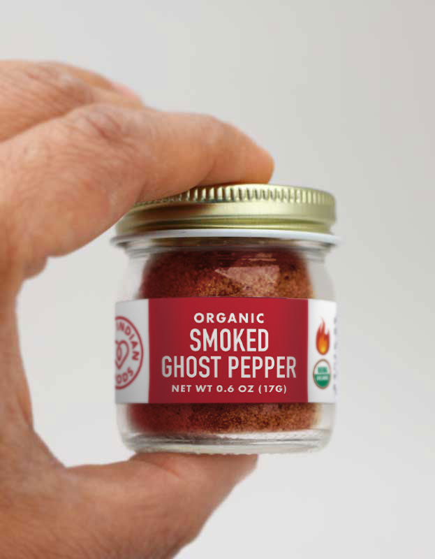A close up of a hand holding a small jar of Organic Smoked Ghost pepper powder from Pure Indian Foods