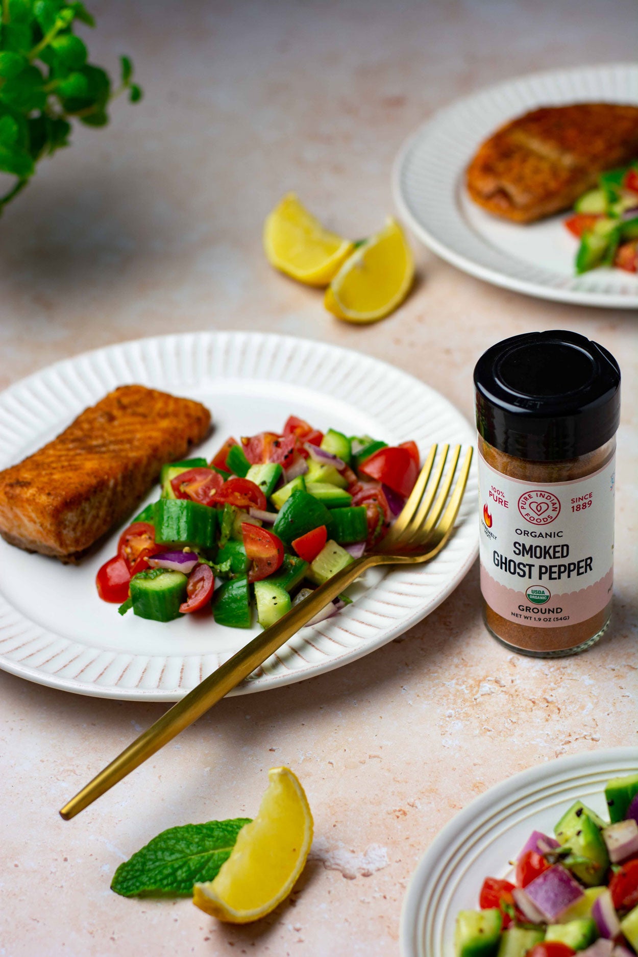 A dinner plate with a serving of salmon steak and fresh vegetables next to a jar of organic ghost pepper powder from Pure Indian Foods