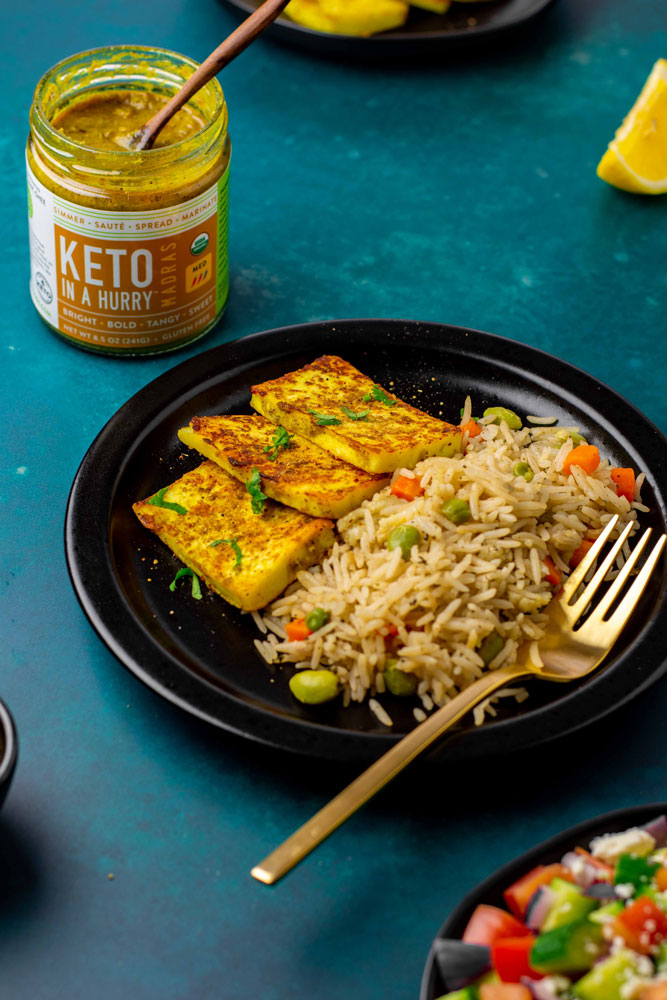 A plate of indian rice pilaf and grilled tempeh made with our keto curry sauce. In the background, there's an open jar of Keto In A Hurry Madras Curry Sauce.