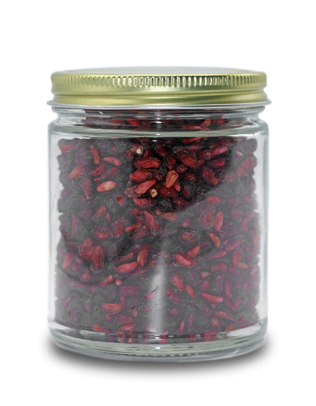 Deep red organic dried pomegranate arils packed in a clear glass jar with a brass colored lid.