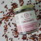 Birds-eye view of a jar of organic Anardana from Pure Indian Foods, resting sideways on a scattering of pomegranate arils