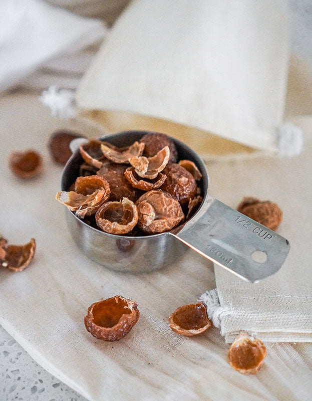 1/2 cup measuring cup full of deseeded organic soap nuts from Pure Indian Foods, pictured next to small muslin bags for laundry.