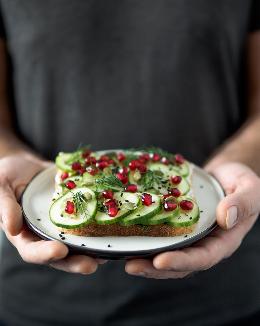 Vegan sandwich made with cucumber, pomegranate arils, fresh herbs, and organic black sesame seeds