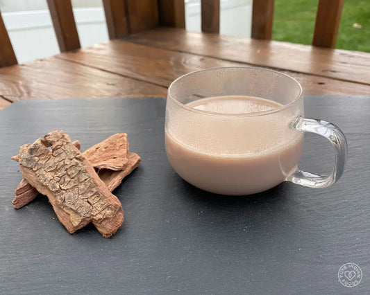 a glass mug of Arjuna milk pictured on a wooden surface next to pieces of arjuna bark