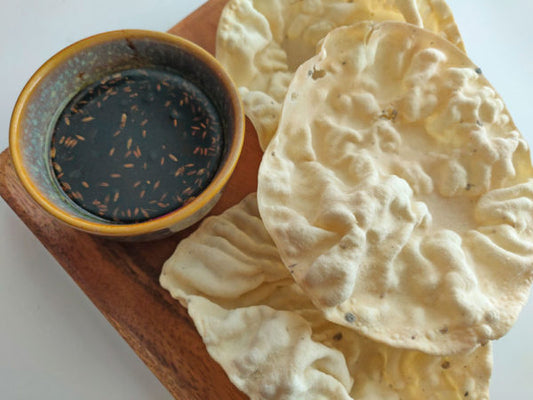 a bowl of tamarind chutney next to a handful of pappadam