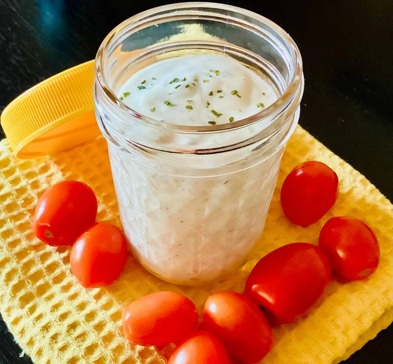 a small jar of vegan ranch dressing surrounded by cherry tomatoes