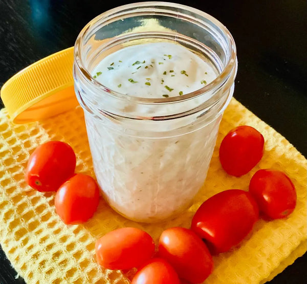 a small jar of vegan ranch dressing surrounded by cherry tomatoes