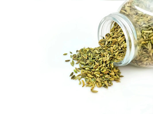 a open glass jar of cumin seeds tipped sideways on a white background with artfully spilled cumin 