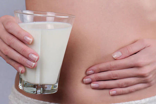 a photo of someone's hand pushing against their stomach while holding a glass of milk