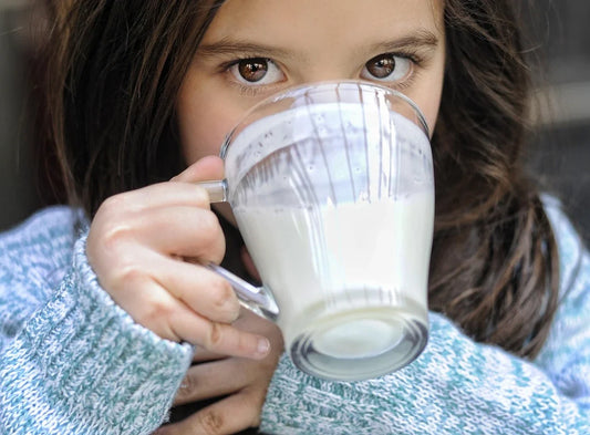 a close up of a brown eyed girl drinking a glass of milk