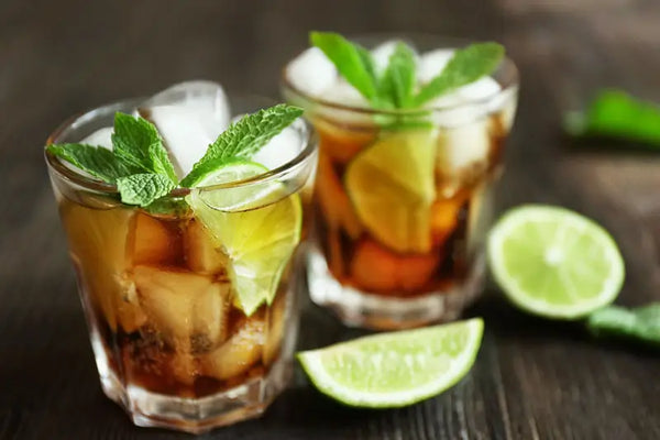 Two glasses of tamarind Ginger Fizz pictured with fresh mint and lime