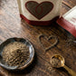 An open bag of organic malabar black pepper from Pure Indian Foods with the ground pepper poured into the shape of a heart on a wooden table.