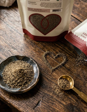 An open bag of organic malabar black pepper from Pure Indian Foods with the ground pepper poured into the shape of a heart on a wooden table.