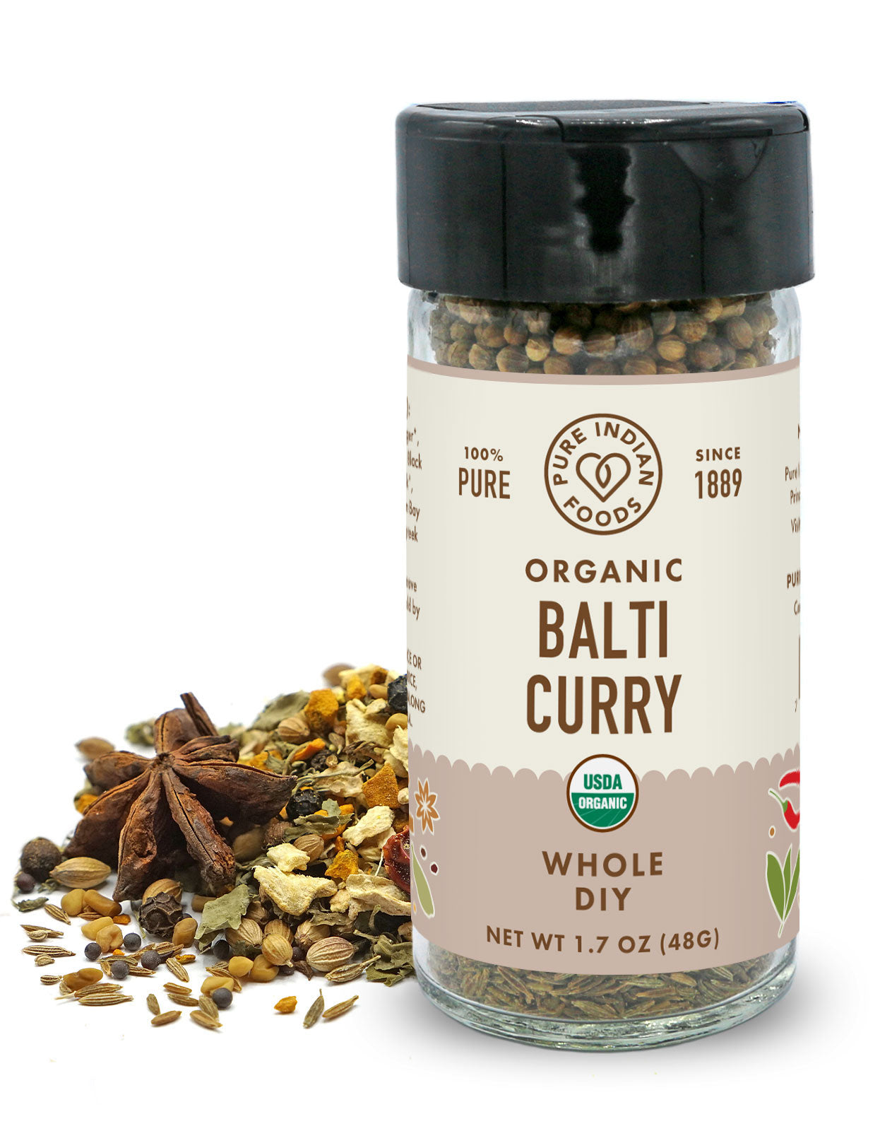 A jar of organic balti curry spice blend placed in front a pile of whole spices on a white background.