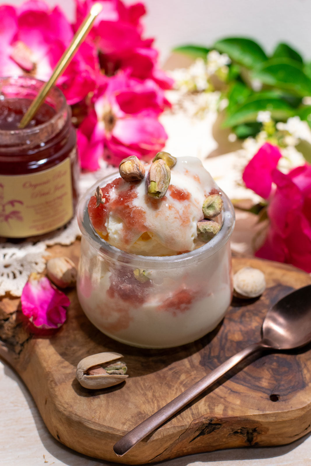 Decadent bowl of ice cream topped with organic rose petal jam, a jar of which is displayed open in the background.