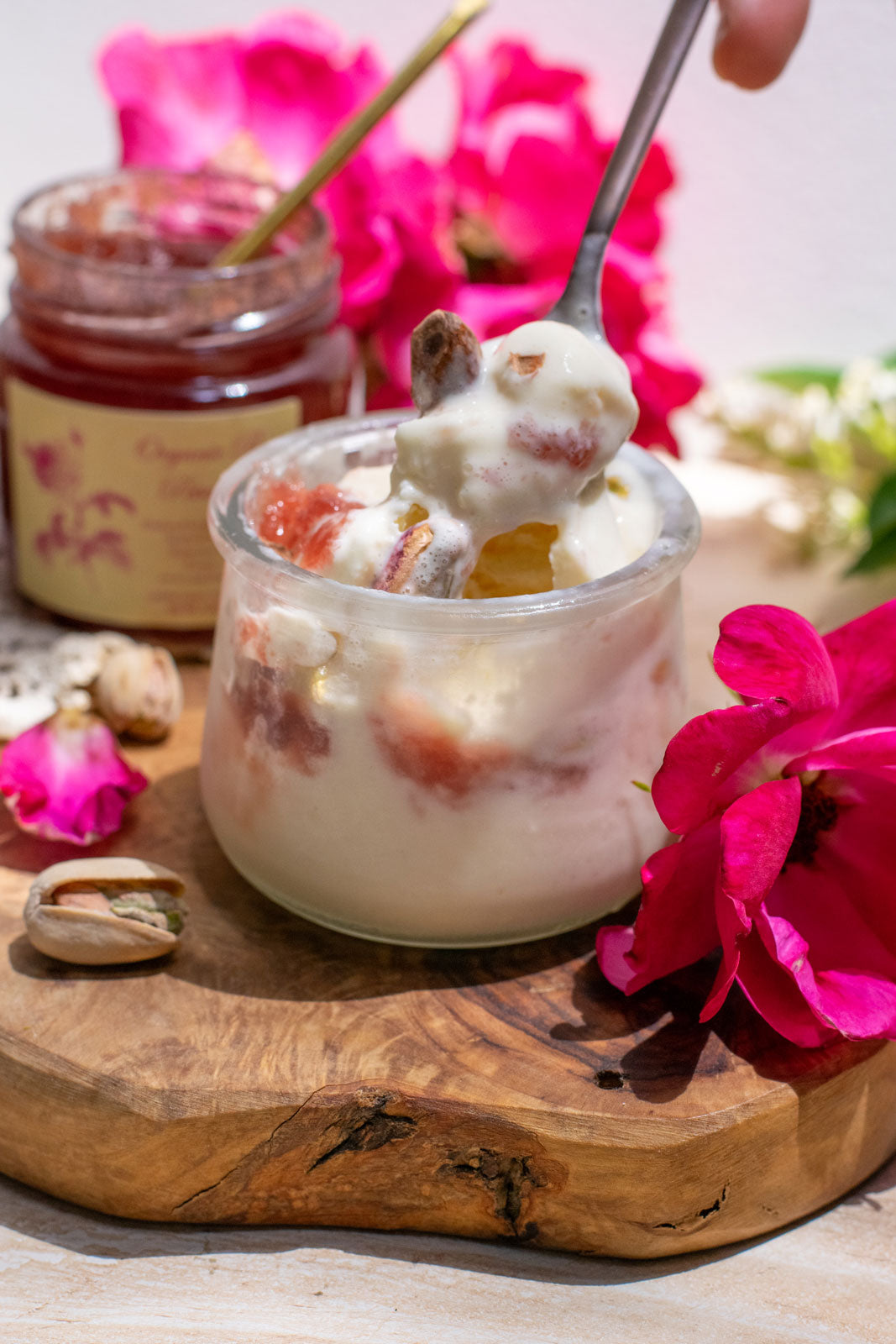 Luxurious spoonful of ice cream topped with organic rose petal jam, a jar of which is open in the background. Displayed next to gorgeous magliano roses.