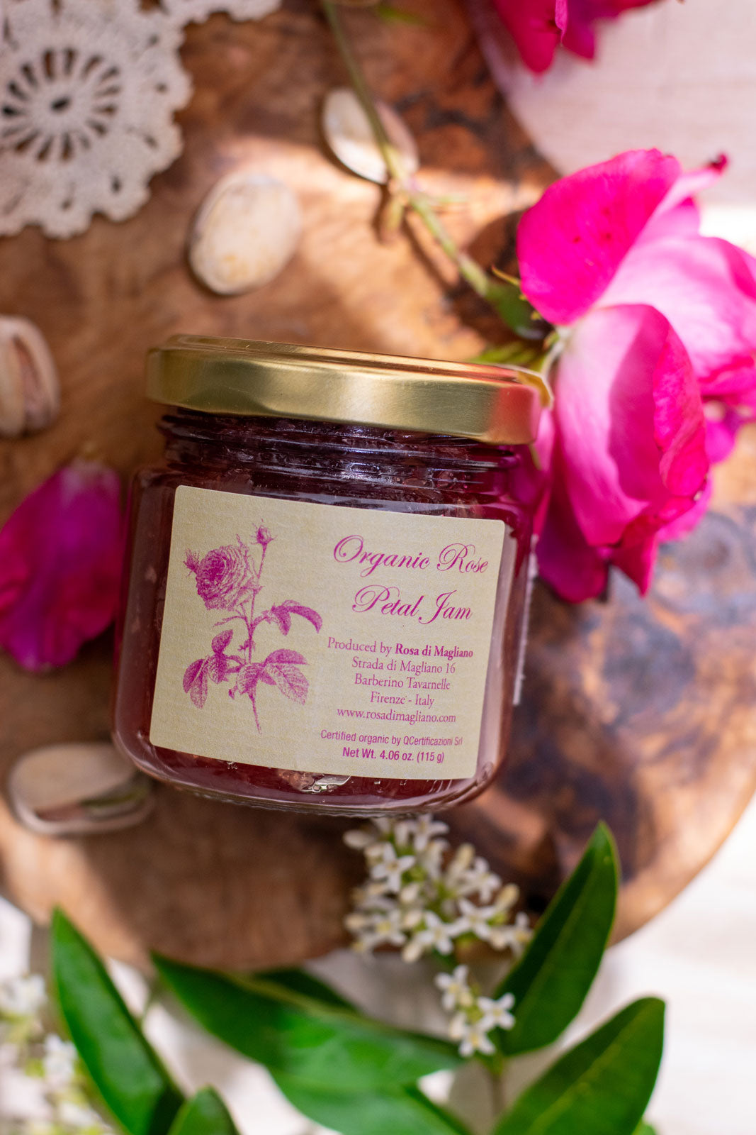 Jar of Organic Rose Petal Jam artfully displayed on a cutting board surrounded by roses and lace