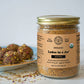 A certified organic ladoo mix that already includes ghee and jaggery, featured in a glass jar in front of a plate of beautiful Ladoos.