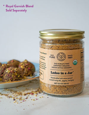 A certified organic ladoo mix that already includes ghee and jaggery, featured in a glass jar in front of a plate of beautiful Ladoos.