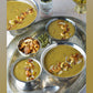 Several silver dishes filled with cooked payasam with a jar of Pure Indian Food organic cardamom pods