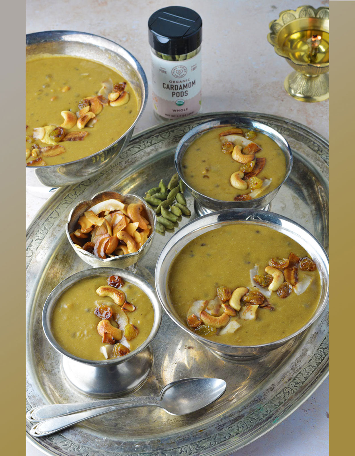 Several silver dishes filled with cooked payasam with a jar of Pure Indian Food organic cardamom pods