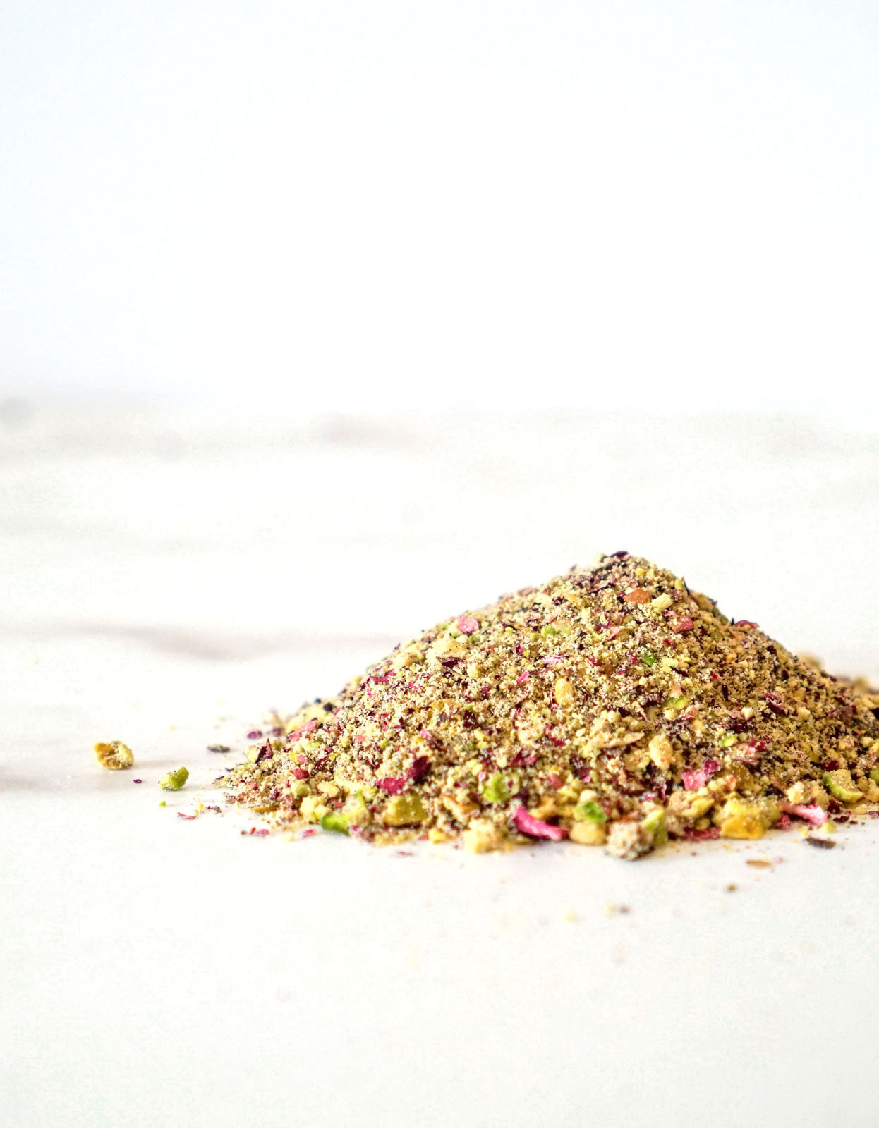 A loose pile of our Royal Garnish Blend made of all-organic ingredients like pistachio, rose petals, saffron, and cardamom on a white marble counter.