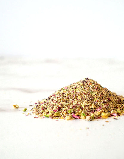 A loose pile of our Royal Garnish Blend made of all-organic ingredients like pistachio, rose petals, saffron, and cardamom on a white marble counter.