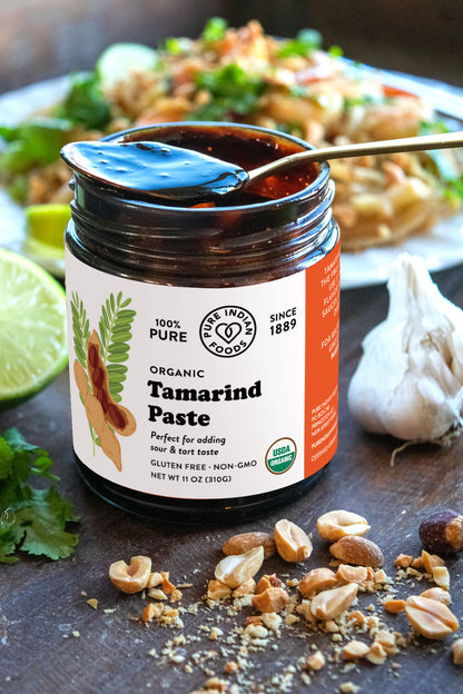 Open jar of organic tamarind Paste from Pure Indian Foods, with a spoon dipped into it. Label says it's perfect for adding sour and tart taste to your food.