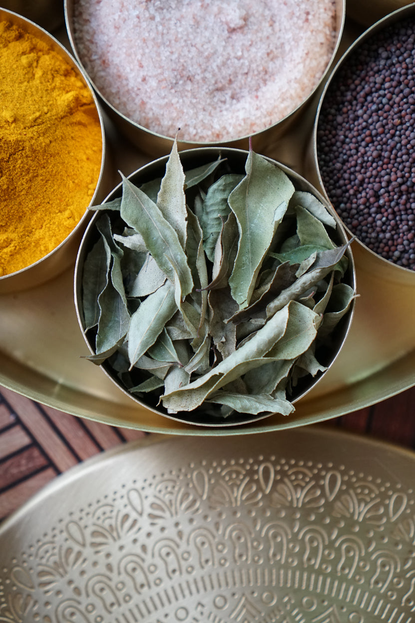 Photo of our dried curry leaves in a brass masala dabba as sold by Pure Indian Foods.