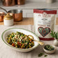 A dish of green bean tomato bhaji on a table runner next to an open bag on Organic Dried Curry Leaves
