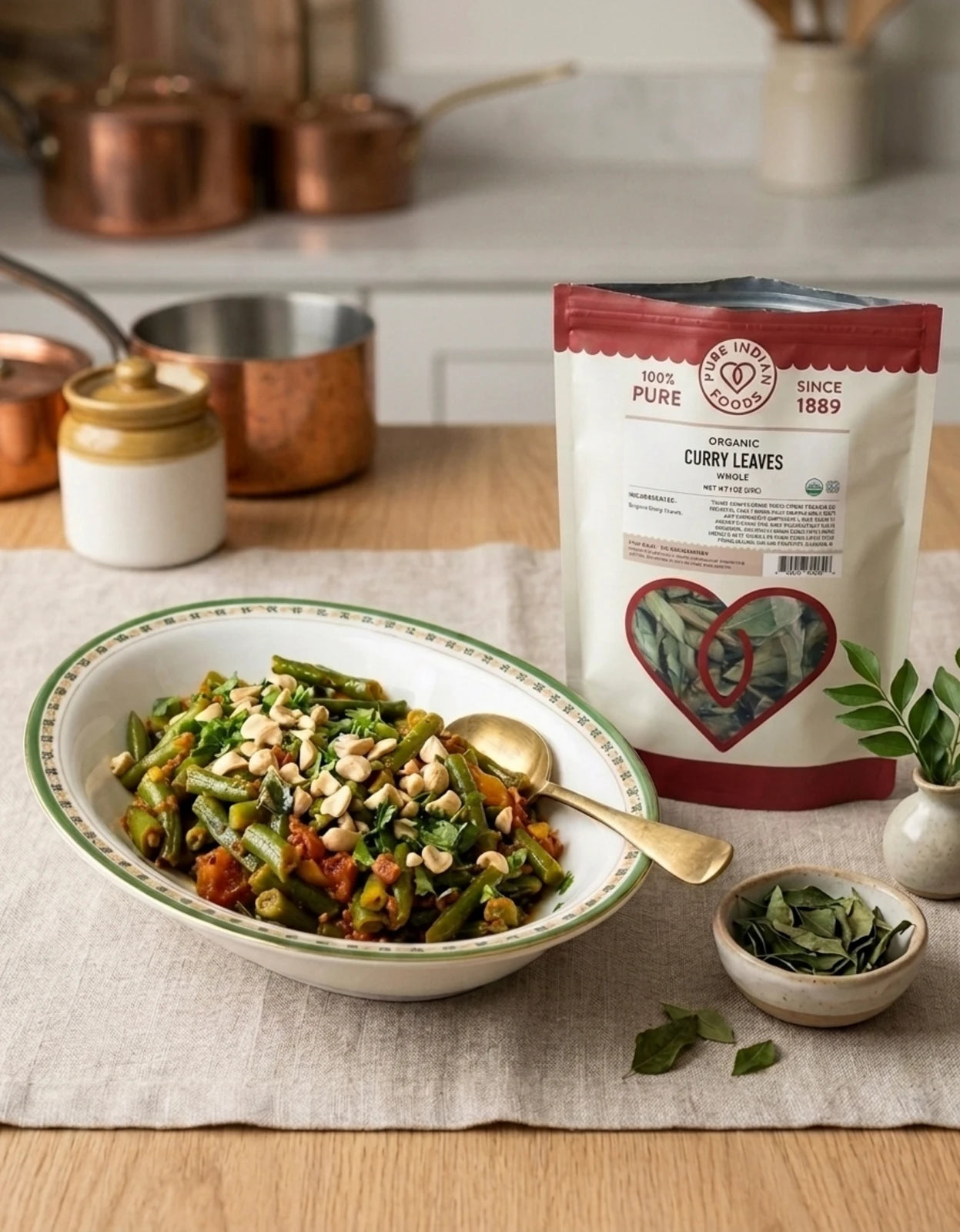 A dish of green bean tomato bhaji on a table runner next to an open bag on Organic Dried Curry Leaves