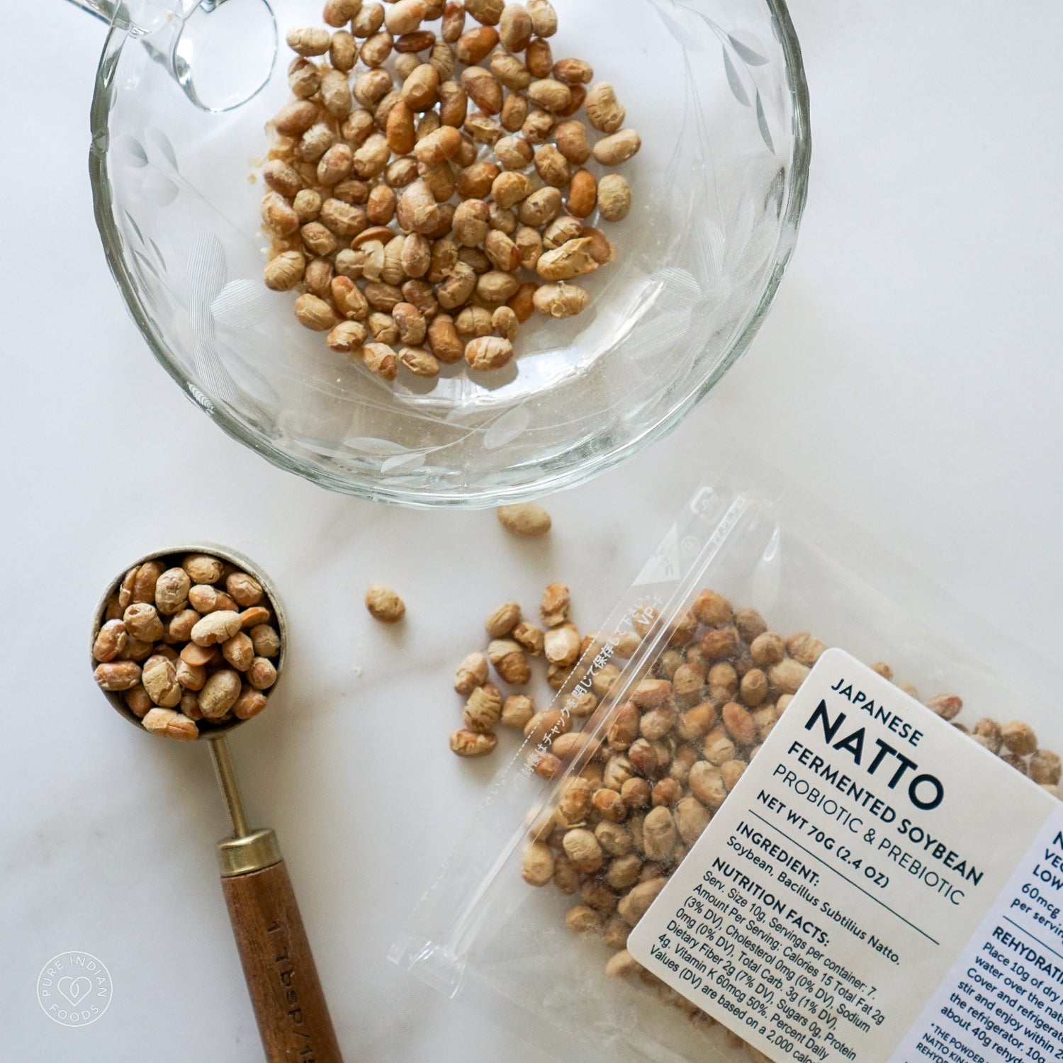 A bag of Pure Indian Foods freeze-dried natto, open with some of the non-gmo natto spilling out. Next to it is a heaping spoonful of the dried natto and a glass bowl filled with even more of the traditionally fermented soybeans.
