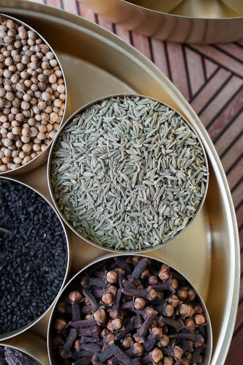 A birds eye view of a brass masla dabba featuring a bowl of whole organic lucknow fennel seeds