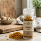 A grinder top bottle of organic coarse granules of turmeric on a wooden counter
