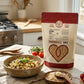 A bag of Organic Sprouted Brown Rice on a wooden table top next to a bowl of cooked rice and chickpeas