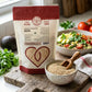 A pouch of Organic Sprouted Quinoa on a wooden board next to a bowl of cooked quinoa salad and a bowl of the uncooked grain