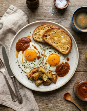 Plate of eggs, toast, and potatoes with a drizzle of our Organic Tomato Chutney on a wooden table.