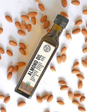 Birds-eye view of a bottle of Cold-Pressed Almond Oil from Pure Indian Foods. Certified Organic. Surrounded by a scattering of almonds.