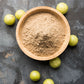 Fine ground organic amla powder in a bowl, surrounded by indian gooseberry (amalaki / amla) fruit.