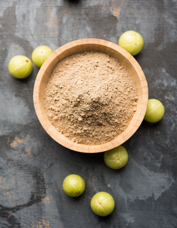 Fine ground organic amla powder in a bowl, surrounded by indian gooseberry (amalaki / amla) fruit.