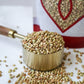 a brass measuring cup overflowing with organic whole buckwheat in front of the product bag from Pure Indian Foods