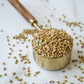 brass measuring cup with a wooden handle filled to overflowing with organic buckwheat