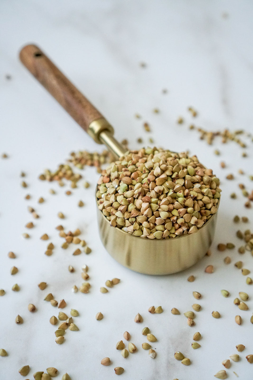 brass measuring cup with a wooden handle filled to overflowing with organic buckwheat