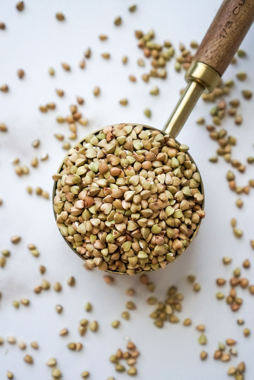 1/3 cup raw buckwheat groats in a brass measuring spoon with a dark wood handle