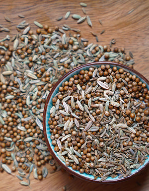 Bird's eye view of our organic CCF tea, scattered on a wooden table top, showing distinct whole seeds of cumin, coriander, and fennel.